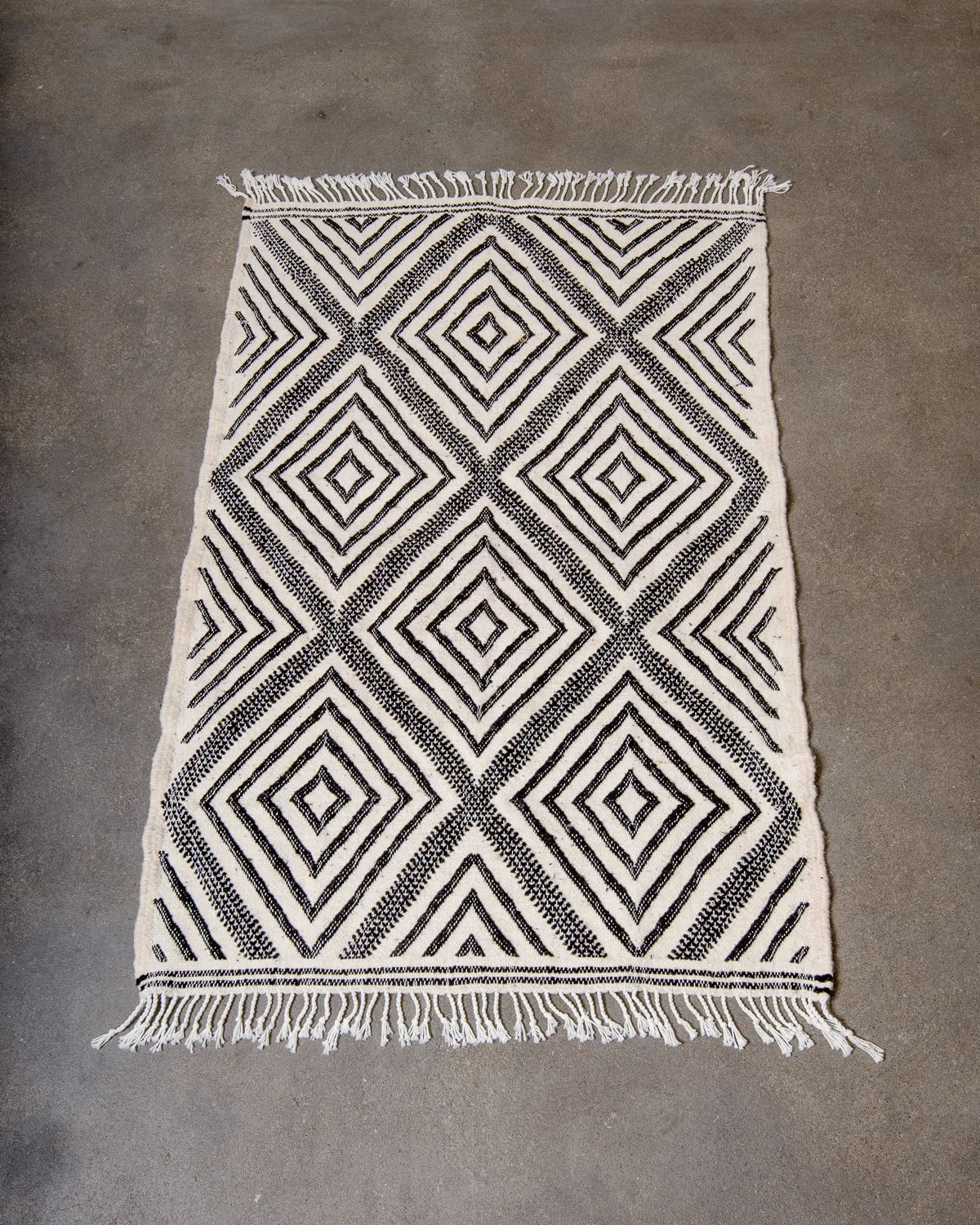 Small Kelim Rug in black and white laying on concrete studio floor.